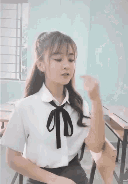a girl in a school uniform is sitting at a desk and holding a piece of paper