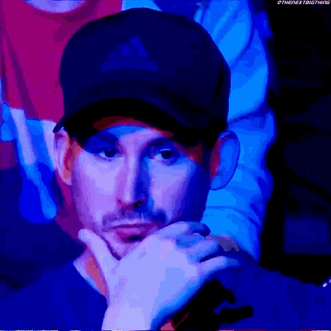 a man wearing a black adidas hat is looking at the camera .