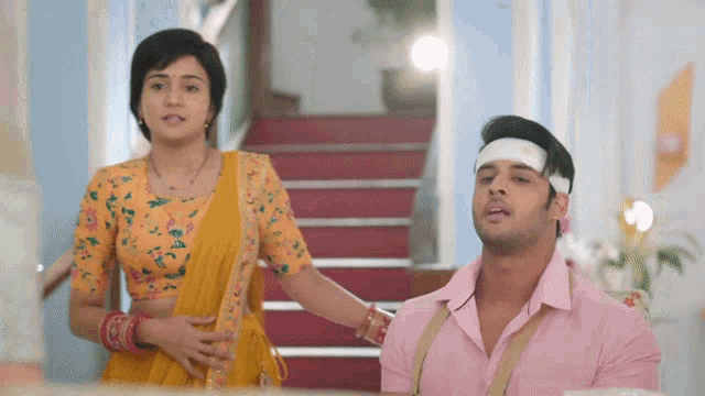 a man with a bandage on his head stands next to a woman in a yellow sari