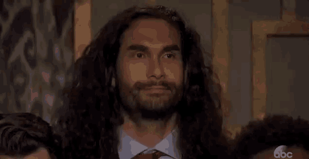 a man with long hair and a beard is standing in front of a crowd of people with his eyes closed .