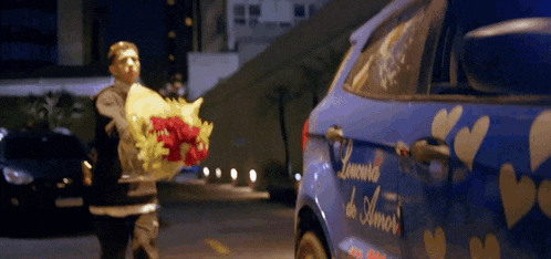 a man carrying a bouquet of flowers stands in front of a blue car that says louania de amor on the side