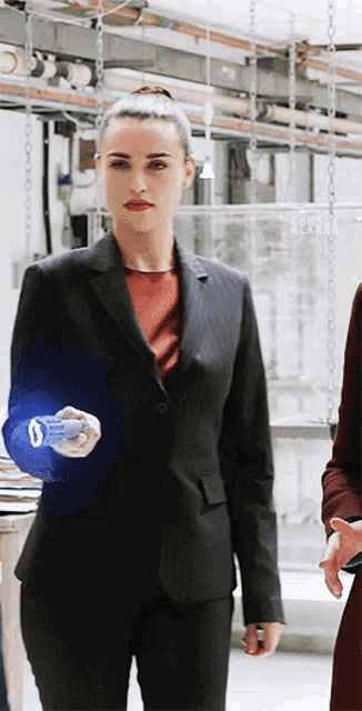 a woman in a black suit holds a blue object in her hand