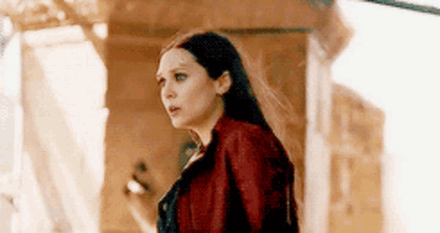 a woman in a red jacket is standing in front of a building and looking at something .