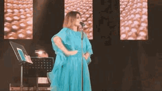 a woman in a blue dress is singing into a microphone while standing on a stage .