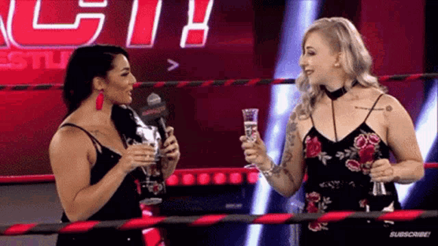 two women are talking to each other in a wrestling ring while holding champagne glasses .
