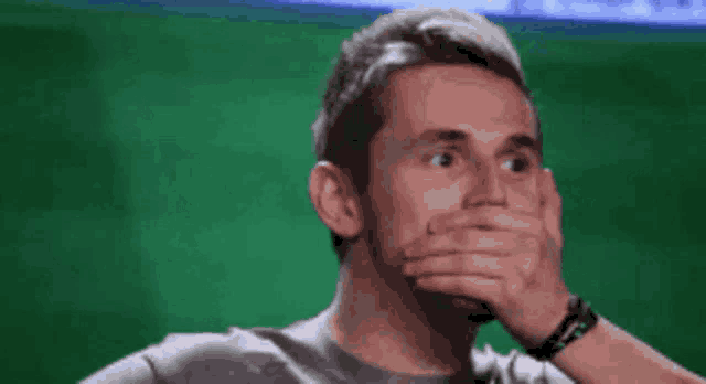 a man covering his mouth with his hand in front of a green background .