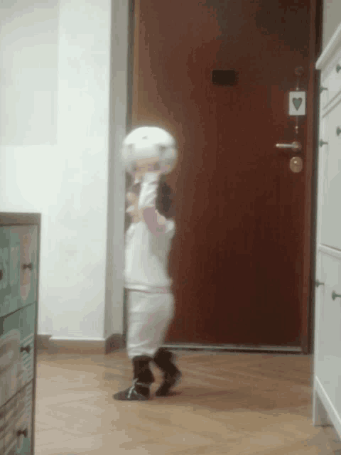 a little girl playing with a soccer ball in front of a door that has a heart shaped sticker on it