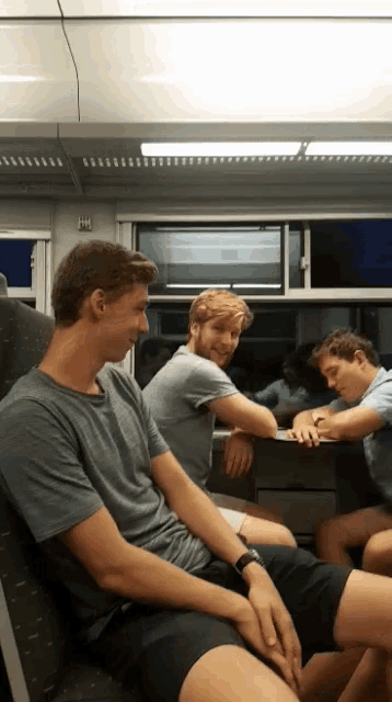 a group of young men are sitting on a train with one wearing a watch