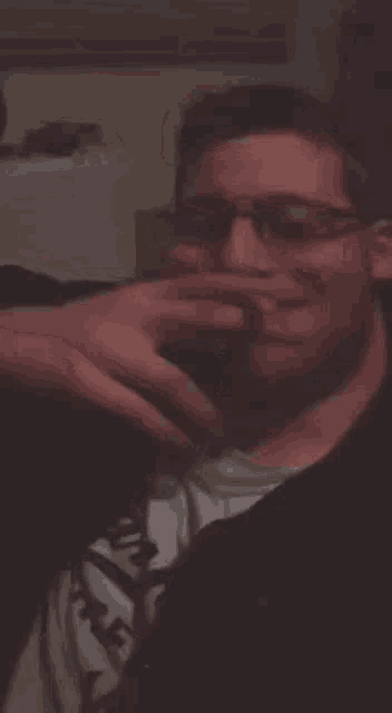 a man wearing glasses and a black shirt is making a funny face in a dark room .