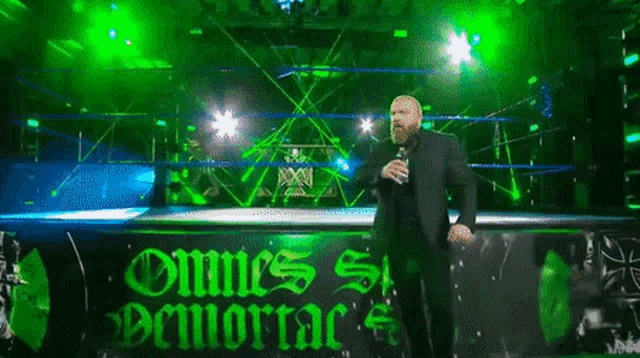 a man in a suit is standing in a wrestling ring with a microphone .