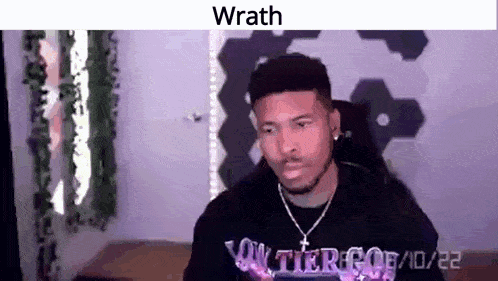 a man with a beard is sitting in a chair in a room with the word wrath on his shirt .