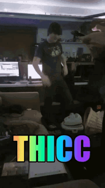 a man in a green shirt is dancing in a living room with the word thicc in rainbow letters