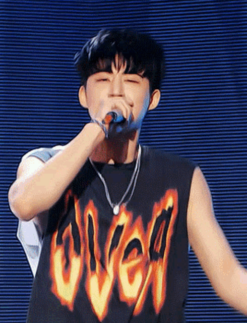 a man singing into a microphone wearing a tank top that says over on it