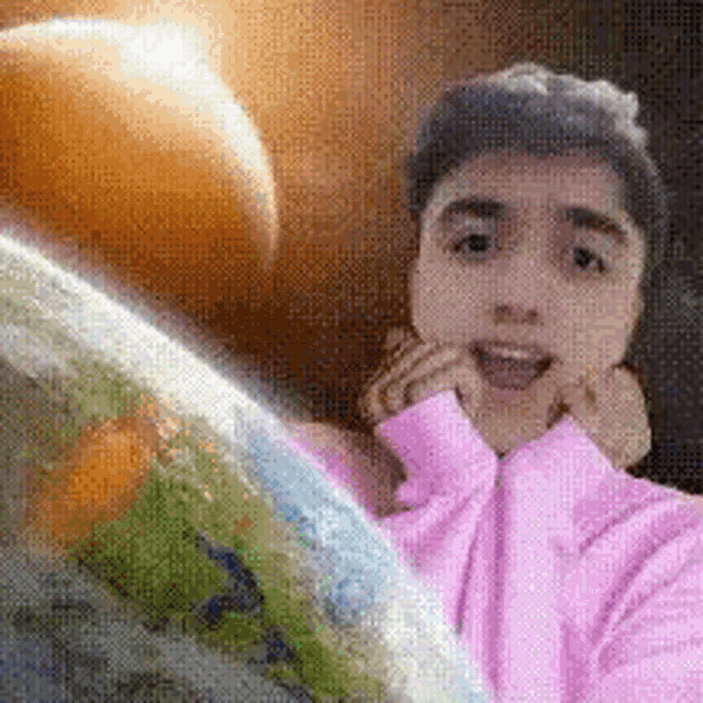 a man in a pink sweater is standing in front of a globe .