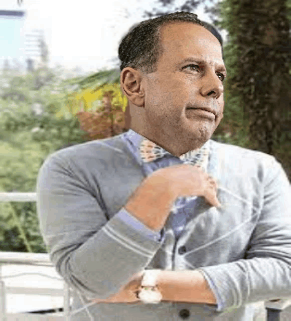 a man wearing a bow tie and a cardigan is sitting with his arms crossed .