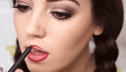 a woman is applying red lipstick with a pencil to her lips .