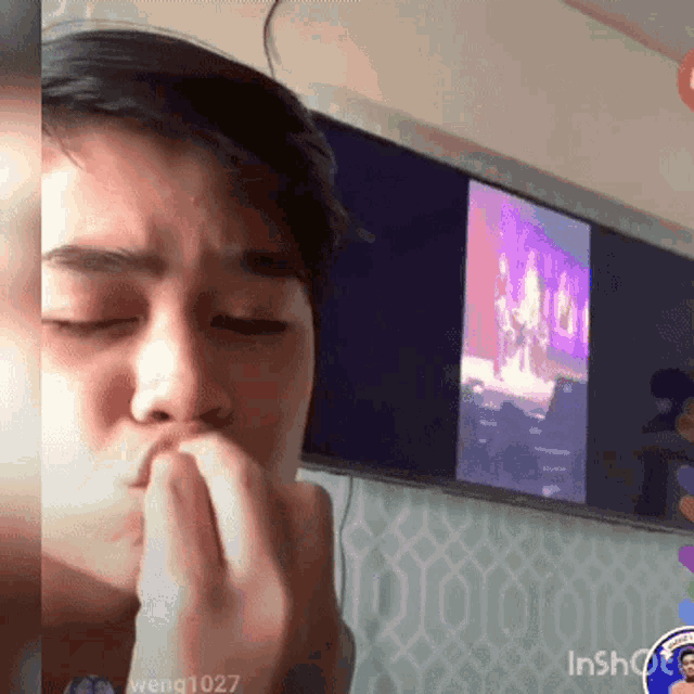 a man covering his mouth with his hand in front of a tv screen that says inshot on it