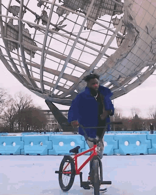 a man in a blue jacket is riding a red bike in front of a globe