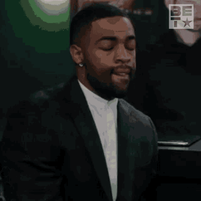 a man in a suit is sitting at a table with his eyes closed and his mouth open .