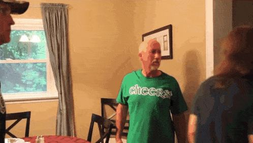 a man in a green cheers shirt stands in a room