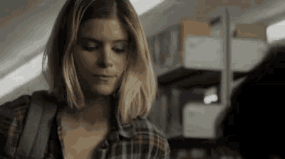 a woman in a plaid shirt is standing next to a man in a room with a backpack .