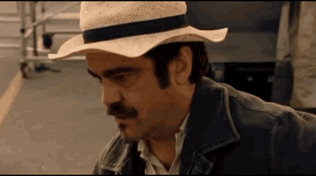 a man with a cowboy hat and a mustache is looking down .