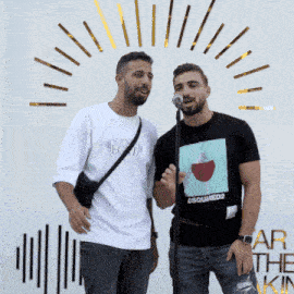 a man wearing a dsquared2 t-shirt stands next to another man singing into a microphone
