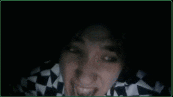 a person wearing a black and white checkered shirt is smiling in the dark .