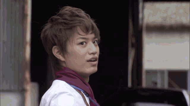 a young man wearing a white shirt and a purple scarf looks at the camera