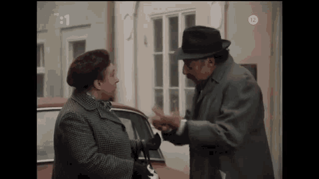 a man and a woman are standing next to each other in front of a car and talking .