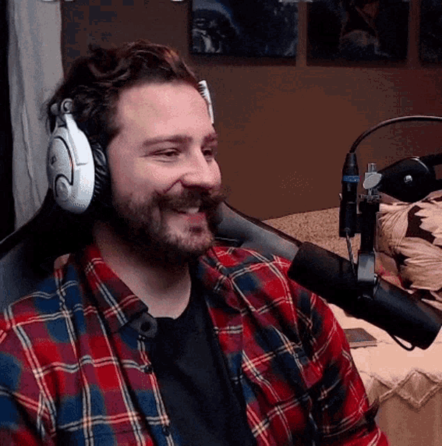 a man wearing headphones and a plaid shirt is smiling in front of a microphone .