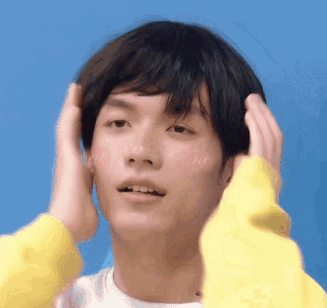 a young man in a yellow sweater is touching his hair