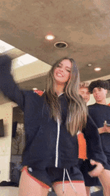 a girl in a black hoodie is dancing in a room with other people