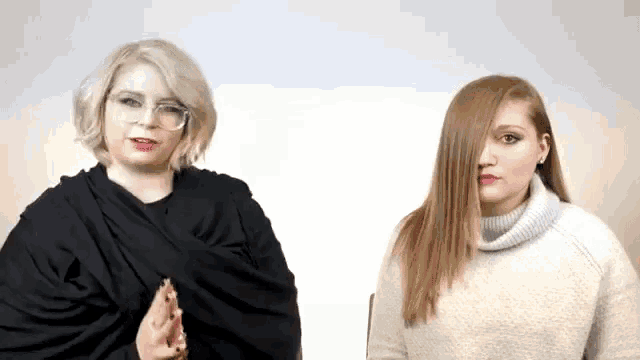 two women are standing next to each other and one is wearing glasses and the other is wearing a sweater .