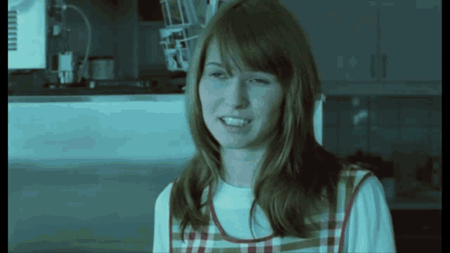 a woman in a kitchen wearing a plaid apron smiles for the camera