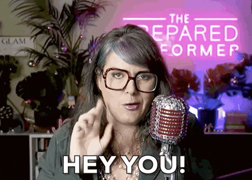 a woman wearing glasses stands in front of a microphone and says " hey you "