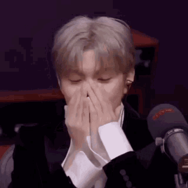 a man in a suit is covering his nose with his hands .