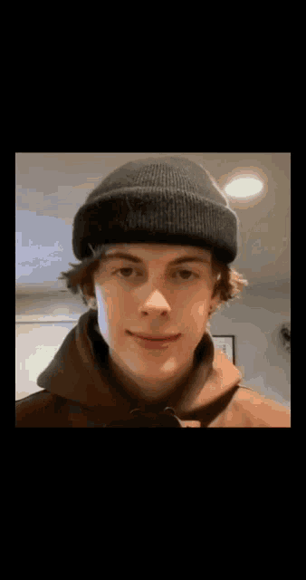 a young man wearing a beanie and a brown hoodie is smiling .