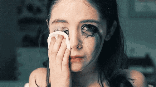 a little girl is crying and wiping her eye with a tissue .