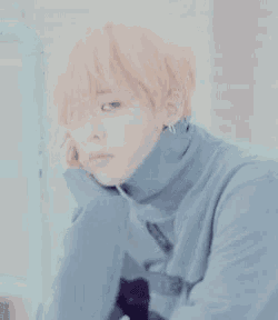 a young man with orange hair is wearing a blue turtleneck sweater and earrings .