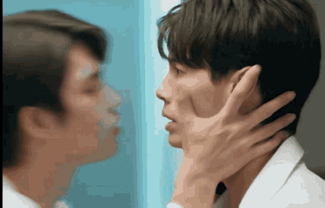 a man 's hand is touching another man 's face in front of a mirror