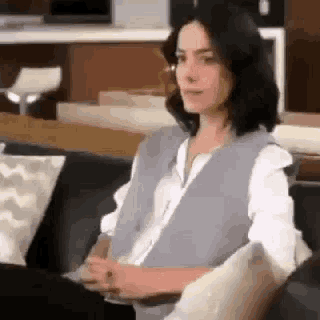 a woman is sitting on a couch in a living room wearing a vest .