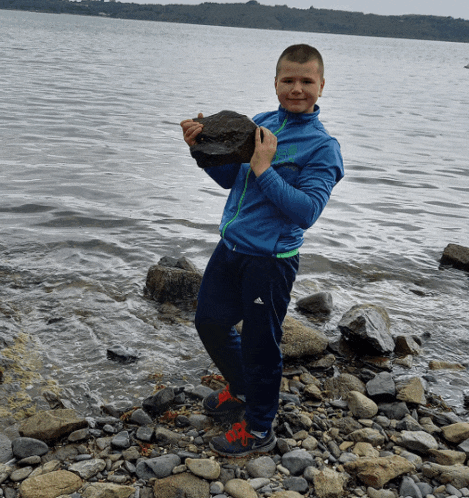 a boy in a blue jacket holds a large rock in his hands
