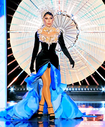 a drag queen is standing on a stage wearing a blue and black dress and a crown .