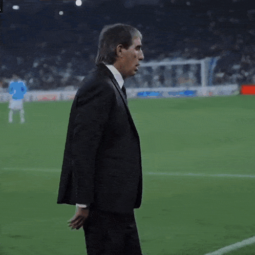 a man in a suit and tie walks on a soccer field