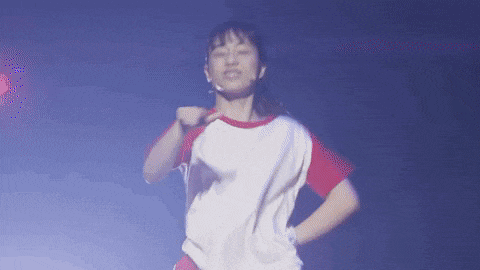 a woman in a red and white shirt is dancing on a stage in a dark room .