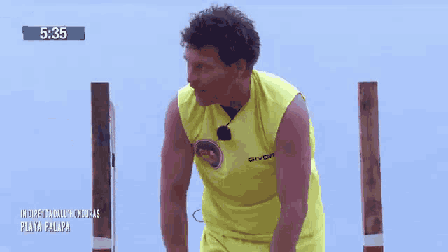a man wearing a yellow givova shirt is standing in front of a wooden pole