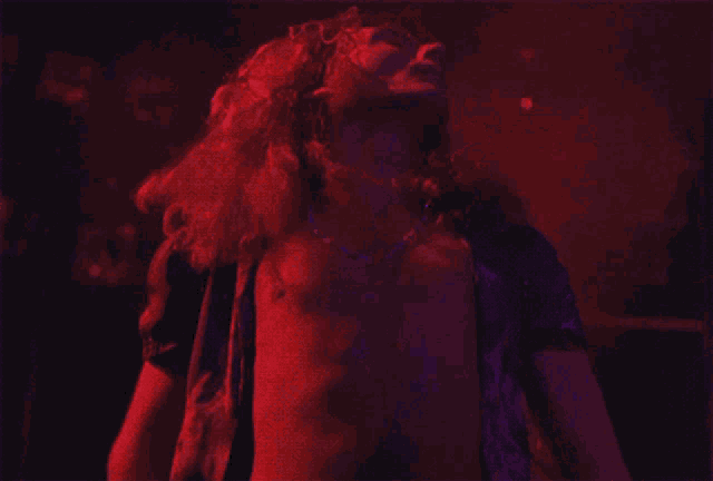 a man without a shirt is dancing in a dark room with purple lights