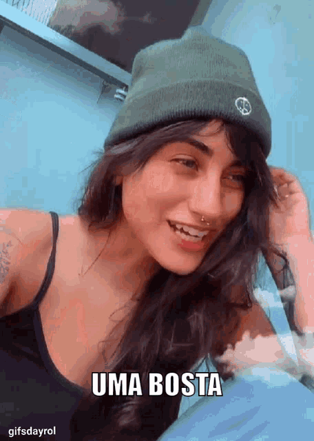 a woman wearing a beanie and a black tank top says uma bosta on the bottom