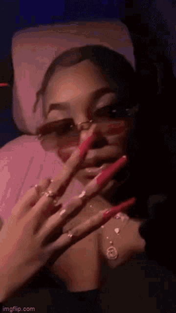 a woman with long red nails is wearing sunglasses and making a peace sign .